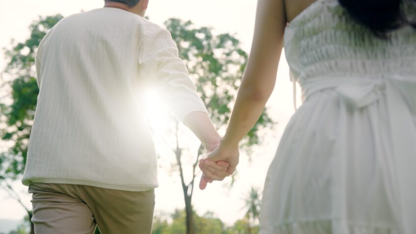 A couple walks hand in hand outdoors on a sunny day