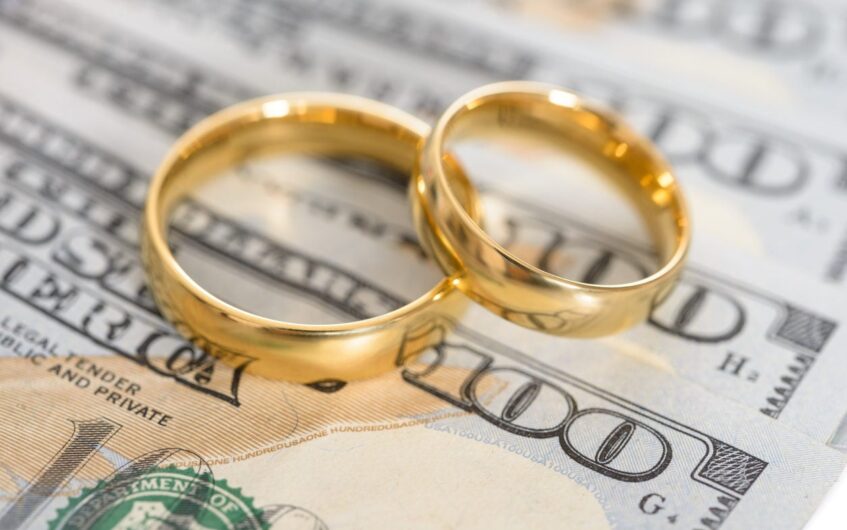 Financial Goals in Marriage. A depiction of wedding bands sitting on a hundred dollars bill