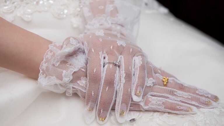 Bride’s sheer lace gloves show her rings against a white bridal dress