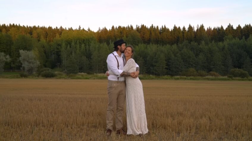 Bride in a crochet wedding dress stands with her groom in an open field