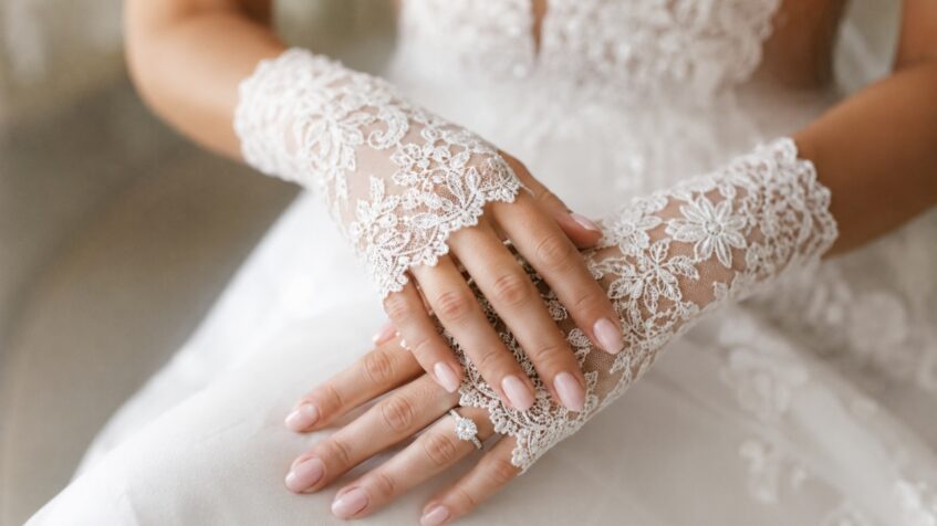 Bride’s fingerless lace gloves frame her ring over a white dress