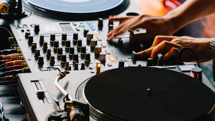 DJ adjusts controls on a mixer beside turntables