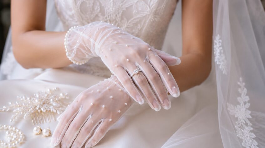 Bride wears pearl tulle gloves with a veil and bridal hair comb nearby