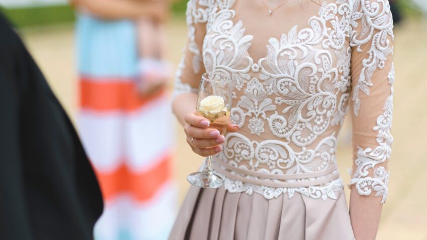 Bride in a lace dress holds a glass at an outdoor ceremony